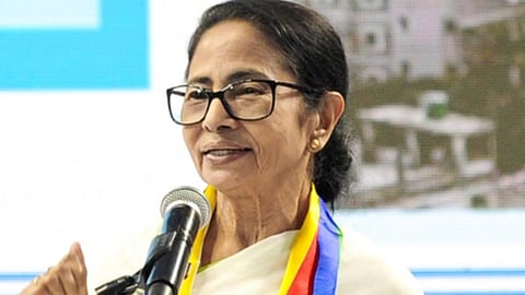 मंच पर माइक्रोफोन के सामने चश्मा पहने एक महिला नेता भाषण देती हुई दिखाई दे रही हैं।