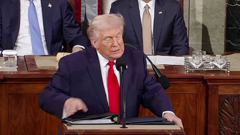 मंच पर माइक्रोफोन के सामने औपचारिक सूट और लाल टाई पहने एक वरिष्ठ नेता भाषण देते हुए दिखाई दे रहे हैं।