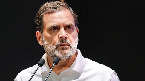 माइक के सामने सफ़ेद टी शर्ट पहने राहुल गाँधी गंभीर मुद्रा में दिखाई दे रहे हैं। 
