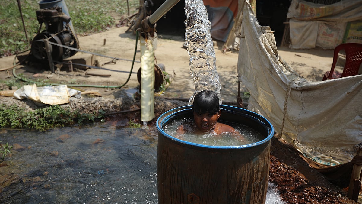A child inside a barrel full of water under the sun outside his hut.  