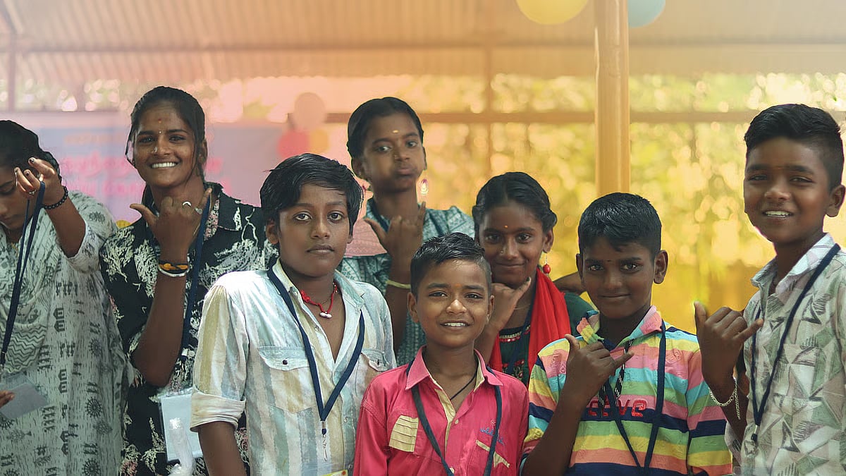 Children at the Theni summer camp pose for a cheerful group photo after a session, flashing hand signs and smiles.