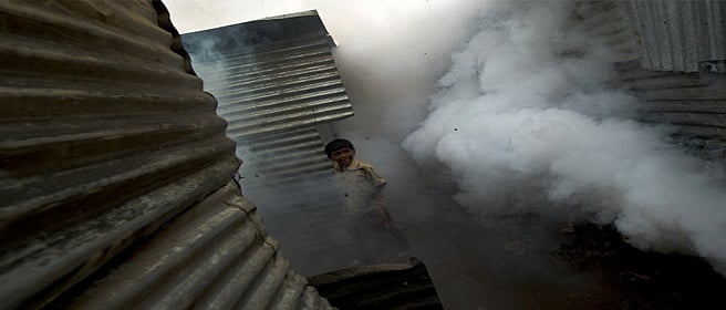 An Indian child plays as a New Delhi Municipal Council (NDMC) worker fumigates construction worker's shanties at the under-construction Shivaji Stadium in New Delhi on August 17, 2010. With the onset of monsoons, municipal authorities have geared up to prevent mosquitoes breeding and combat water-borne diseases in the Indian captial ahead of the Commonwealth Games. AFP PHOTO/ MANAN VATSYAYANA (Photo credit should read MANAN VATSYAYANA/AFP/Getty Images)