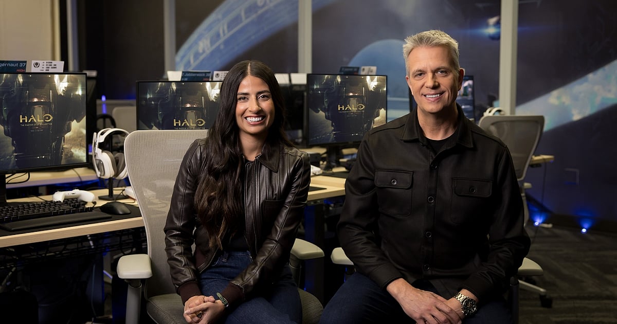 Asha Sharma and Matt Booty seated in a gaming studio with Halo: The Master Chief Collection displayed on monitors behind them