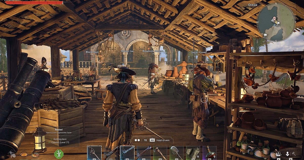 A third-person gameplay screenshot of Windrose showing a player character in pirate attire standing inside a wooden, open-air workshop filled with crafting tables, cannons, and supplies. Other NPC crew members are visible in the background under a thatched roof, with a detailed HUD showing inventory items like sabers and flintlocks.
