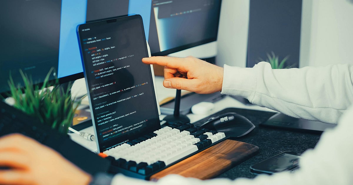 A programmer working on code with a laptop and monitor setup in an office
