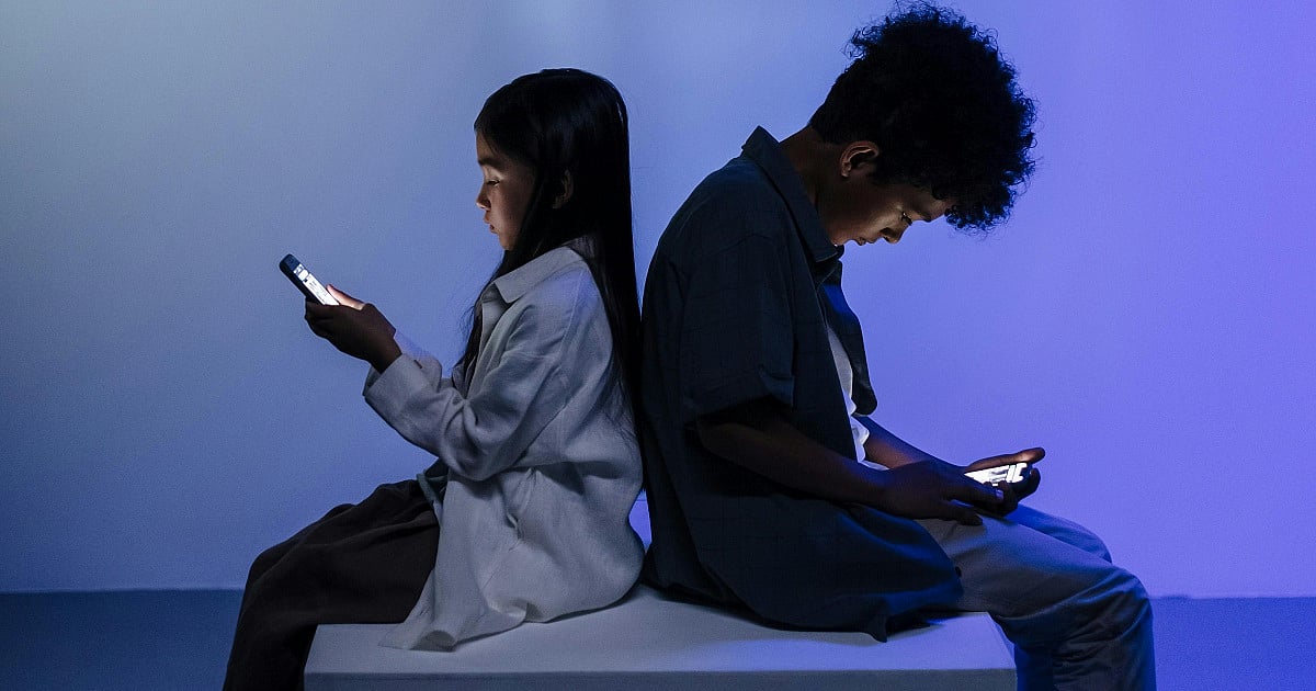 Two children facing away from each other, engaged with smartphones