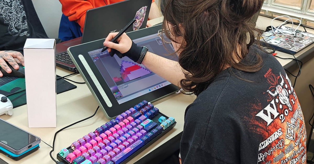 A game developer working on a digital art project using a professional pen display tablet and a mechanical keyboard with vibrant purple and pink backlighting