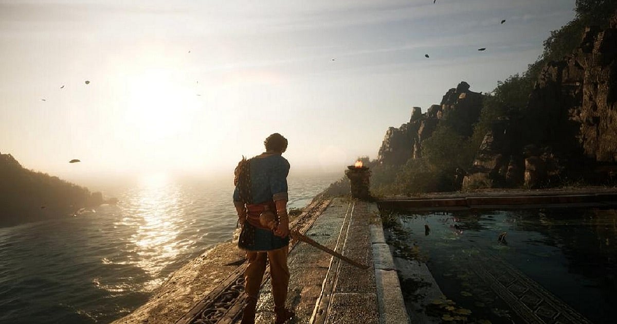 Gameplay screenshot from Unleash the Avatar showing protagonist Vikram standing on a stone walkway overlooking a sunlit sea at sunset. Wearing a blue tunic and carrying a sword at his side, he faces the glowing horizon while rocky cliffs, a tranquil reflecting pool, and a lit brazier frame the scenic, ancient Indian-inspired environment.