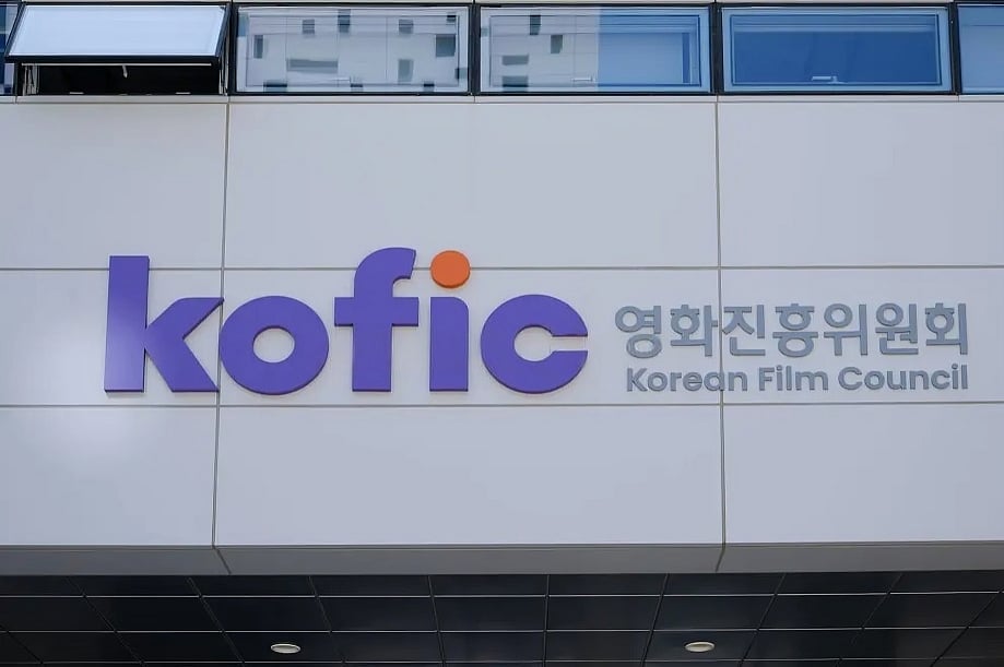 The exterior signage of the Korean Film Council mounted on a light grey paneled building wall. On the left, a large, bold purple logo displays the lowercase letters "kofic" with a bright orange dot over the letter 'i'. To its right, grey lettering features the Korean title "영화진흥위원회" positioned directly above the English name "Korean Film Council".