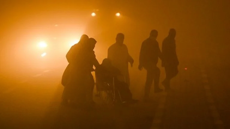 A wheelchair-user is helped across a road in dangerously low visibility in the southern Iraqi city of Basra on April 14. - null