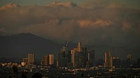 Plumes of smoke from wildfires, including the Bridge Fire, are seen in the mountains behind the downtown Los Angeles skyline at sunset as seen from Kenneth Hahn Park in Baldwin Hills, Los Angeles, California, on September 10, 2024