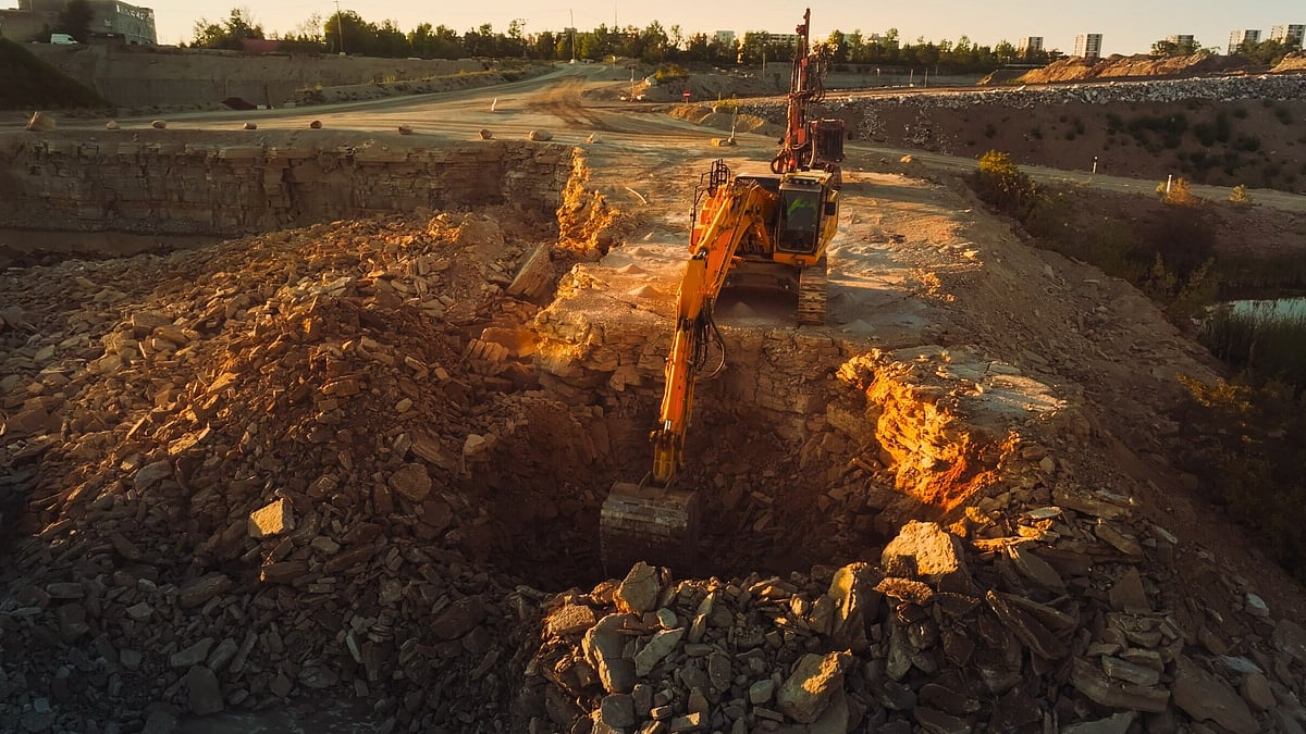 Excavator at work in an open-pit mining site during sunset, revealing layers of mineral-rich earth - null