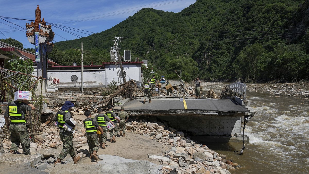 Soldiers carry relief supplies for the trapped villagers passing by a road damaged by flood after heavy rains, in Miyun district on the outskirts of Beijing - Image by Xinhua News Agency