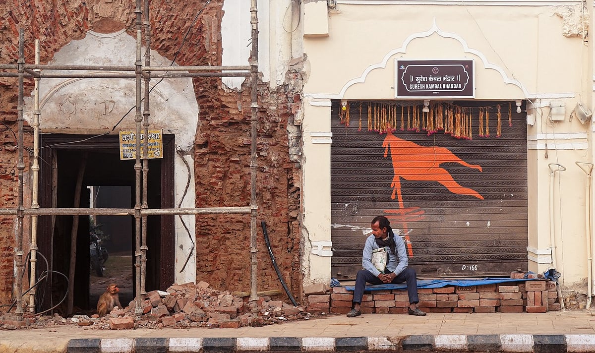 PTI/Manvender Vashist Lav : A man sits near a shop whose shutter has been decorated with Hindu-theme artwork ahead of January 22