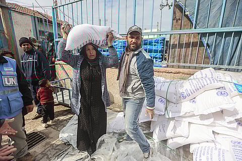 Palestinians, who left their homes and took refuge in Rafah city under hard conditions, carry the flour they received from UNRWA.