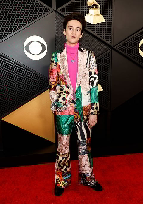 Singer-songwriter Jacob Collier in a colorful patchwork suit paired with a pink turtleneck and blue flower necklace.