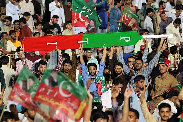 Getty Images : Supporters of Pakistani cricket star-turned-politician and head of the Pakistan Tehreek-e-Insaf (PTI) Imran Khan holds a giant cricket bat with the colours and initials of the party | 