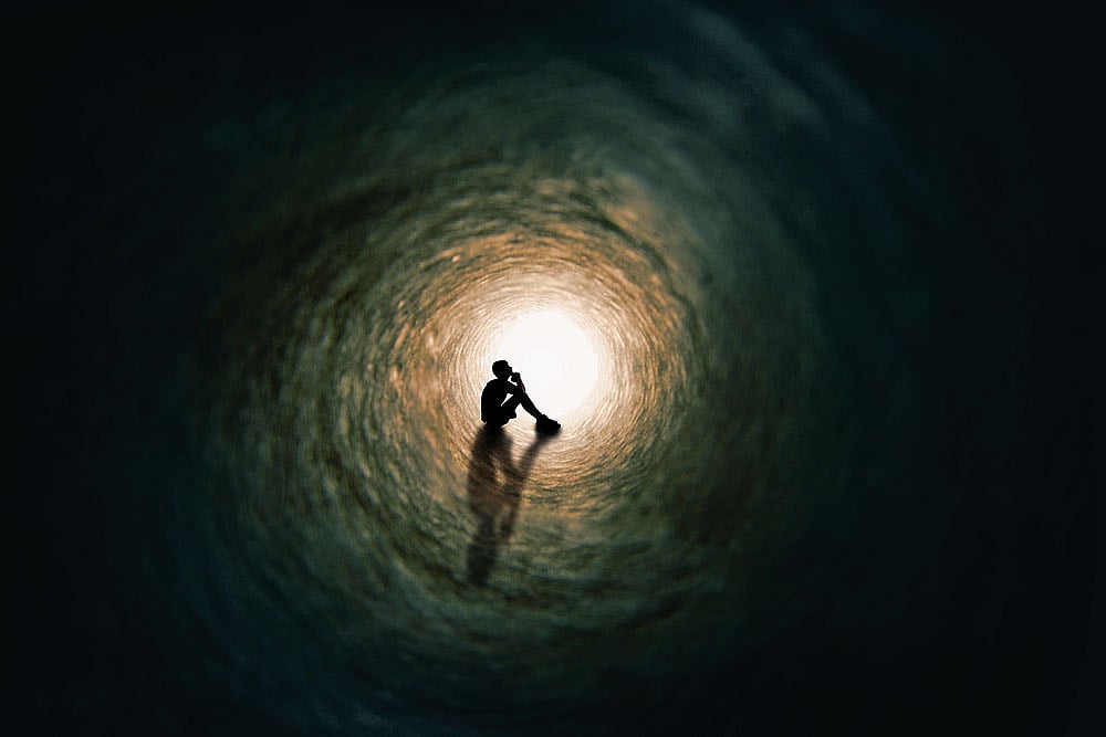 Photo: Getty Images : The silhouette of a teenage boy sitting and praying at the end of a tunnel with a bright light at the end 