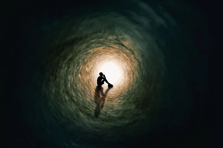 Photo: Getty Images : The silhouette of a teenage boy sitting and praying at the end of a tunnel with a bright light at the end