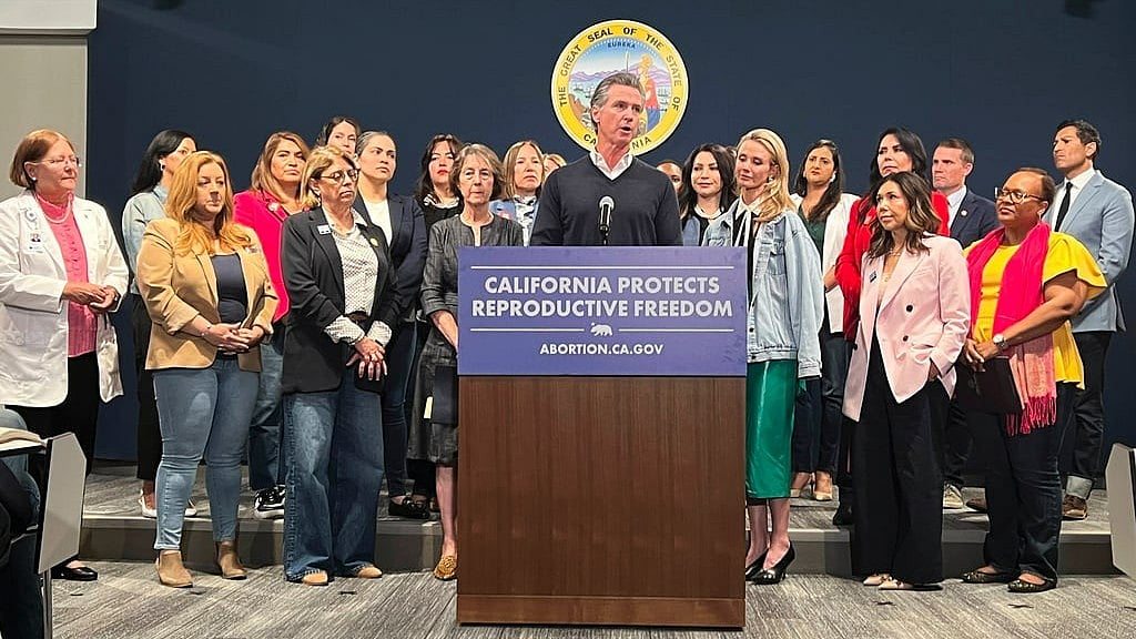 AP : Joined by the state Legislative Women's Caucus and advocates, California Gov. Gavin Newsom, center, speaks during a news conference, Wednesday, April 24, 2024, in Sacramento, Calif., to announce legislation that would help Arizona women access abortions. The proposal would circumvent a ban on nearly all abortions in Arizona by allowing Arizona doctors to give their patients abortions in California. 