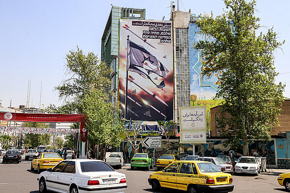 (Photo by ATTA KENARE via Getty Images)
 : Vehicle move past a building showing a banner depicting missiles and drones flying past a torn Israeli flag, with text in Persian reading "the next slap will be harder" and in Hebrew "your next mistake will be the end of your fake state", in Palestine Square in Tehran on April 14, 2024