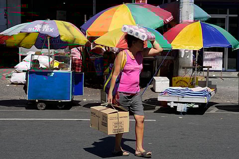 A woman uses tissue paper rolls to shield her from the scorching sun as she crosses a street in Quezon city, Philippines on Tuesday, April 2, 2024.