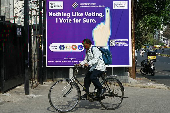 NOAH SEELAM/AFP via Getty Images : A man rides past an election awareness poster displayed along a street ahead of India's upcoming general elections, in Hyderabad on March 26, 2024