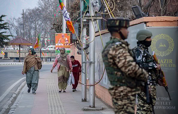 Women walk along a street adorned with Bharatiya Janata Party (BJP) flags and boards, while Indian paramilitary troopers stand alert ahead of Prime Minister Narendra Modi's visit. -  (Photo by Idrees Abbas via Getty Images)