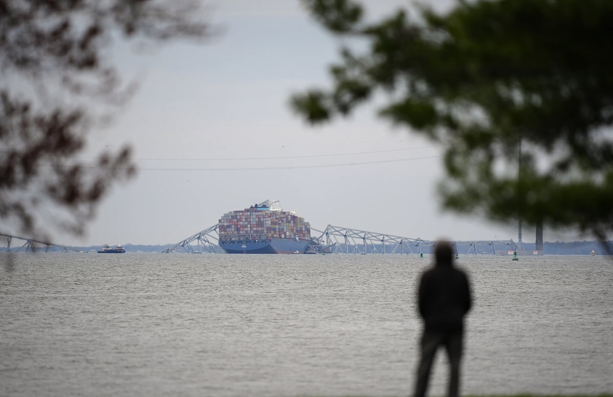 A person views from Fort McHenry a container ship as it rests against the wreckage of the Francis Scott Key Bridge.  - AP