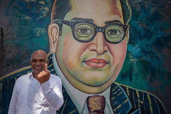 Getty Images : Jaishankar M., 55, stands in front of a mural of the Indian social reformer and political leader Bhimrao Ramji Ambedkar and shows his finger marked with indelible ink after voting in the second phase of the general elections on April 26, 2024 in Bengaluru