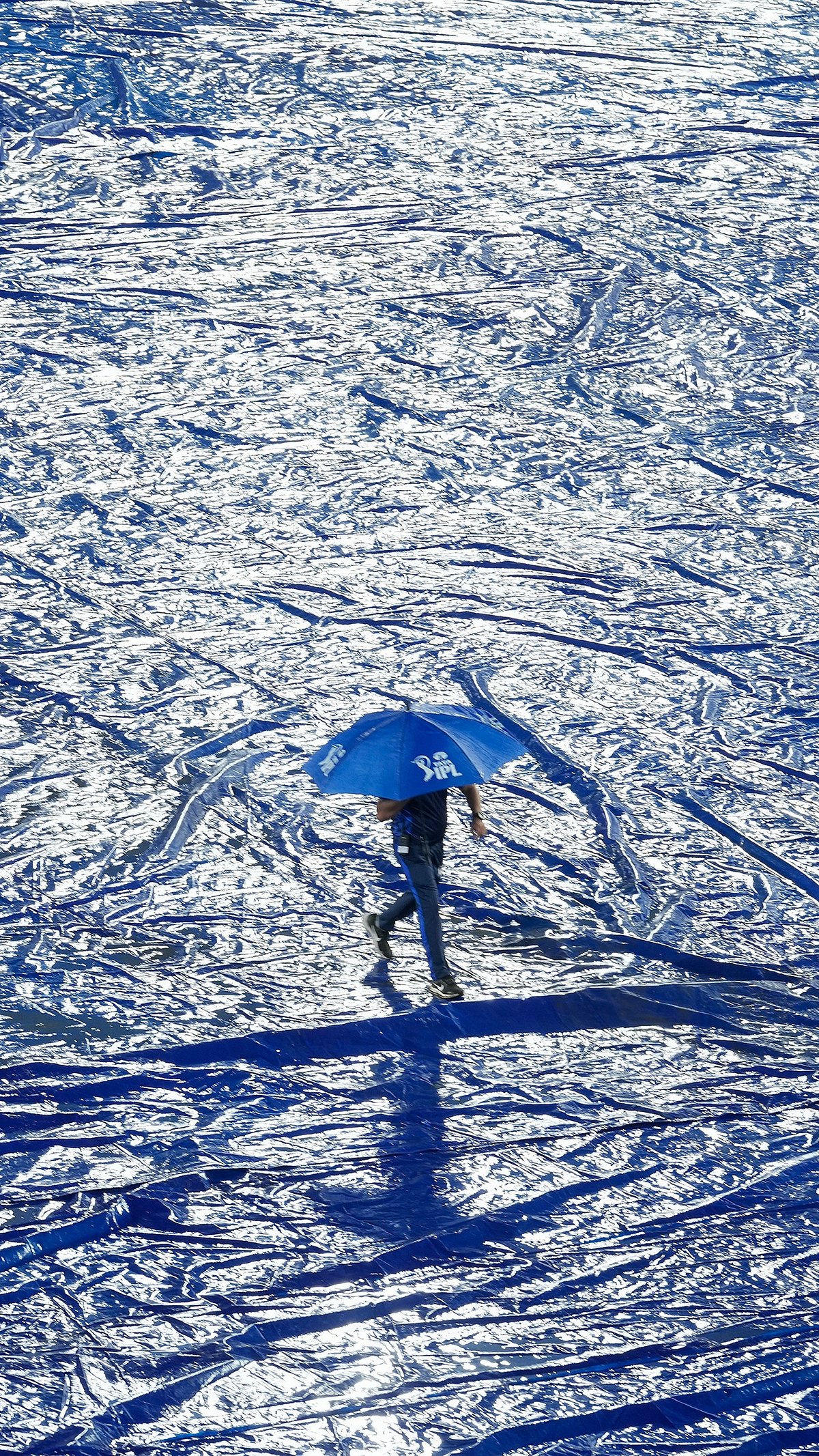 A ground staff walks with an umbrella during rain before the start of the Indian Premier League cricket match between Gujrat Titans and Sunrisers Hyderabad in Hyderabad. - AP Photo