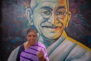 Getty Images : K. S. Gowramma, 65, stands in front of a mural of Indian freedom fighter Mohandas Karamchand Gandhi and shows her finger marked with indelible ink after voting in the second phase of the general elections on April 26, 2024 in Bengaluru, India.