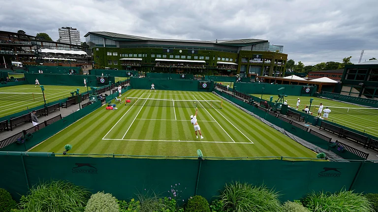 Tennis players train as a member of ground staff waters the plants at the All England Lawn Tennis and Croquet Club in Wimbledon, London, Friday, June 28, 2024. The Wimbledon Championships begin on July 1. - (AP Photo/Kirsty Wigglesworth)