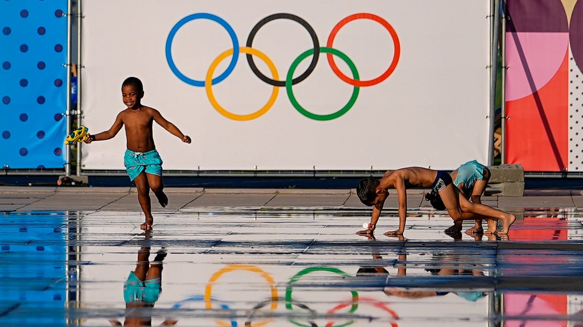 AP Photo/Julio Cortez : Children play at a splash fountain area near signage for the 2024 Summer Olympics in Nice, France.