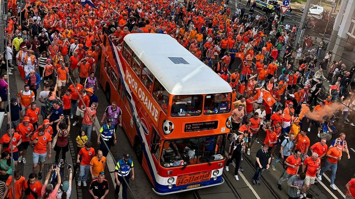 X : Dutch soccer fans in orange outfits with iconic orange double-decker bus.