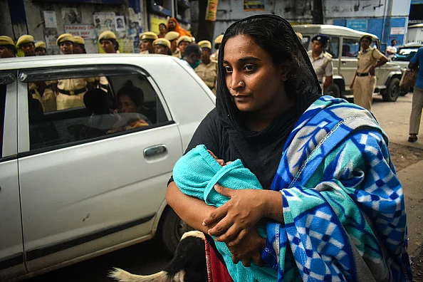 A woman is carrying her newborn baby and walking outside of the Emergency ward