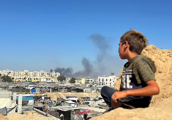 A Palestinian child hides near the rocks as smoke rises from the Hamed area following an Israeli attack Palestinian child hides near the rocks as smoke rises from the Hamed area following an attack