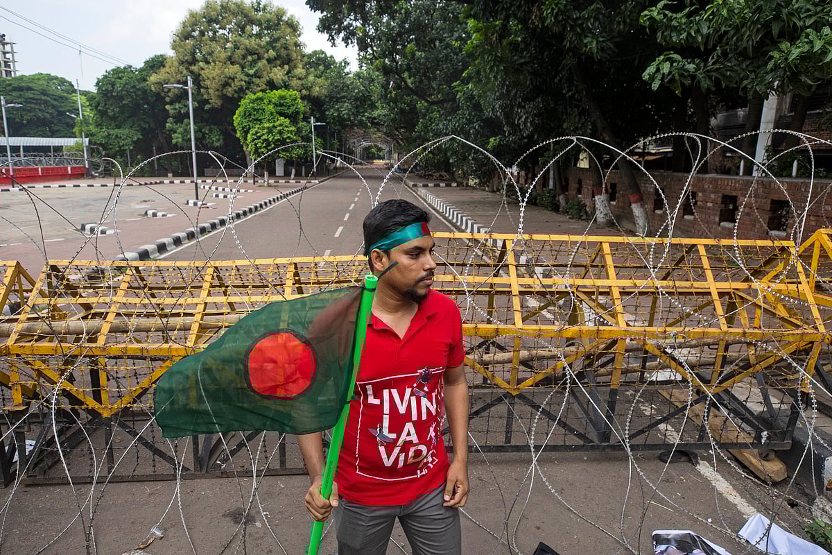 (AP Photo/Rajib Dhar) : A protester carries Bangladesh flag as he and others block the road in front of the former residence of Sheikh Mujibur Rahman