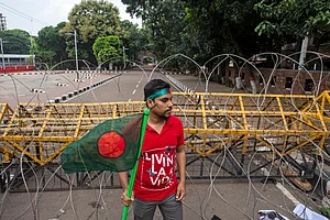 (AP Photo/Rajib Dhar) : A protester carries Bangladesh flag as he and others block the road in front of the former residence of Sheikh Mujibur Rahman