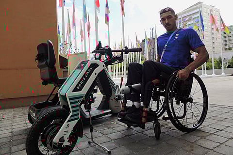Qatari para athlete Ali Radi Arshid poses near a motorized device that pulls wheelchair users in the Paralympic Games Village in Saint-Ouen, France.
