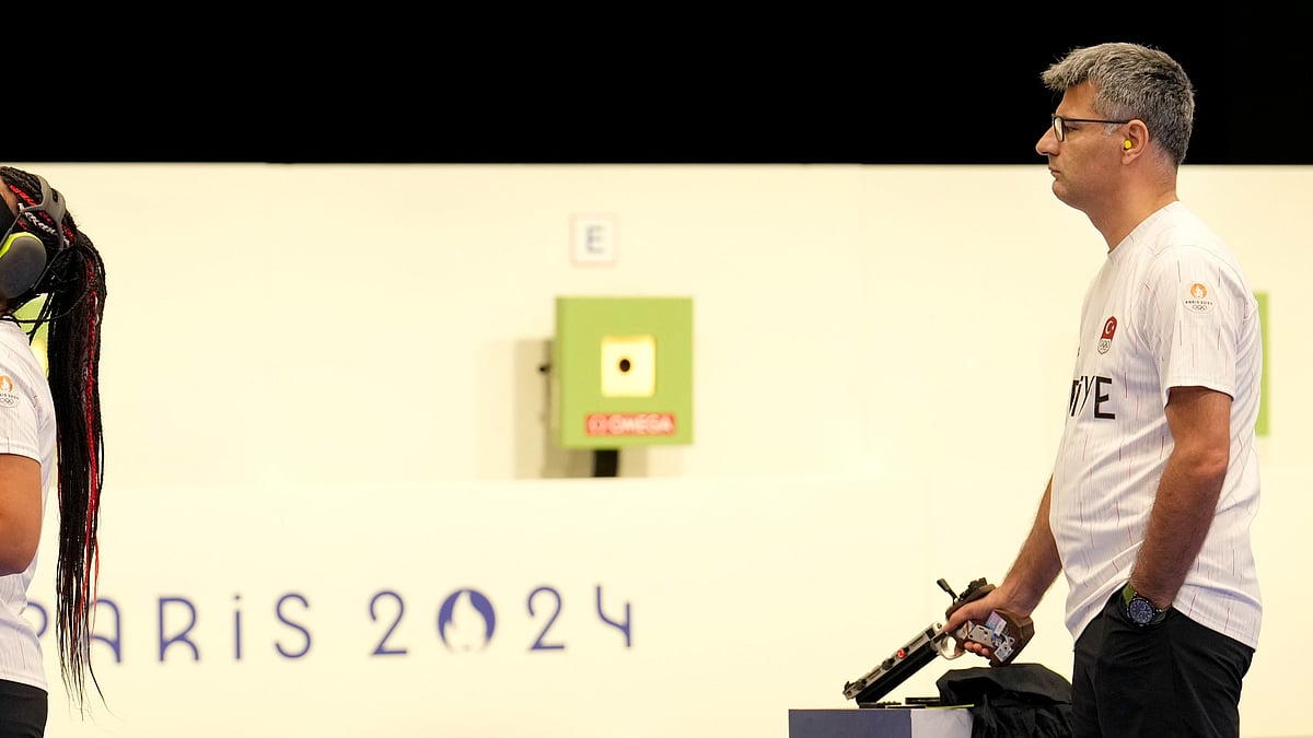 (AP Photo/Manish Swarup) : Turkish shooter Yusuf Dikec, right, looks on as Turkey's coach talks to Dikec's teammate Sevval Ilayda Tarhan during a time-out break at the 10m air pistol mixed team final, in Chateauroux, France, at the 2024 Summer Olympics, Tuesday, July 30, 2024. The Turkish team won the silver medal. 