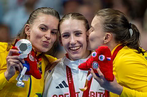 Paralympic athlete Louise Fiddes, of Great Britain, celebrates at the podium with Debora Borges Carneiro, left, and Beatriz Borges Carneiro, right, after winning at Women's 100 m Breaststroke -SB14 final, during the 2024 Paralympics, Monday, Sept. 2, 2024, in Paris, France.