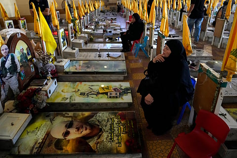 Women sit in a cemetery as they visit the graves of killed Hezbollah members in the southern suburbs of Beirut, Thursday, Sept. 19, 2024