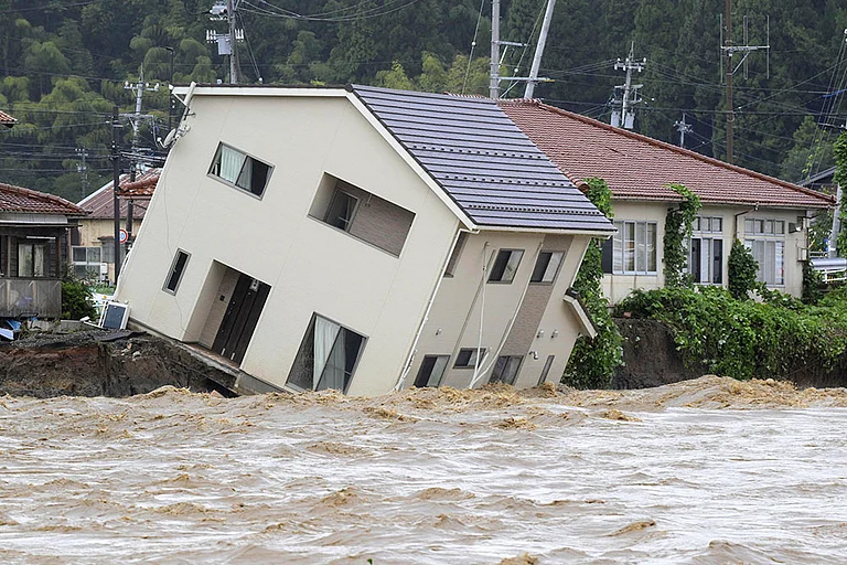 Japan Floods: A house leans as a swollen river undermines the ground in Suzu - | Photo: Kasumi Fukudome/Kyodo News via AP