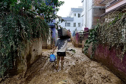 Nepal Floods: A man walks on a muddy alleyway carrying belongings salvaged from his house