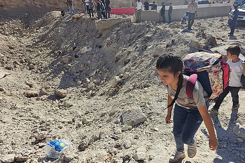 Mideast Tensions: A girl carries her belongings crossing on foot into Syria through a crater caused by an Israeli airstrike