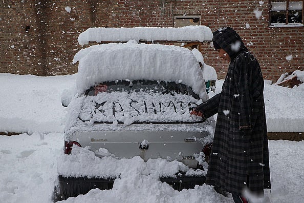 A man writes on the back window of a car during a heavy snowfall in Srinagar, Kashmir, India, February 22, 2022.  - Kashmir beneath snow 
