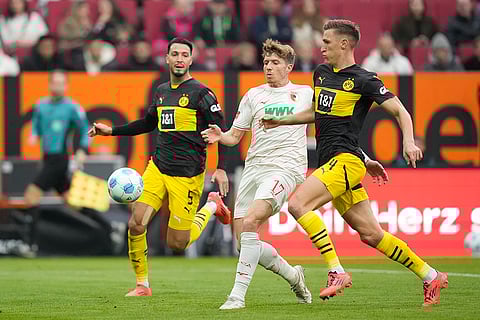 Bundesliga soccer: Augsburg's Kristijan Jakic, centre, challenges for the ball with Dortmund's Nico Schlotterbeck, right, and Ramy Bensebaini