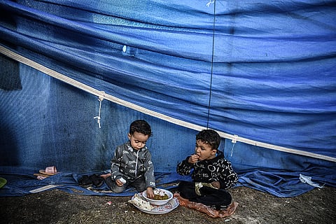 Palestinian children who displaced to the area around Nasser Hospital eat food distributed by volunteers