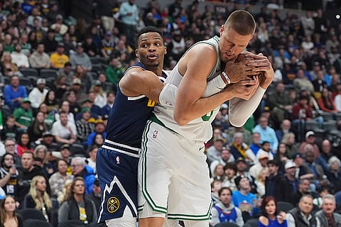 NBA 2024-25: Celtics center Kristaps Porzingis, right, collects a loose ball as Nuggets guard defends